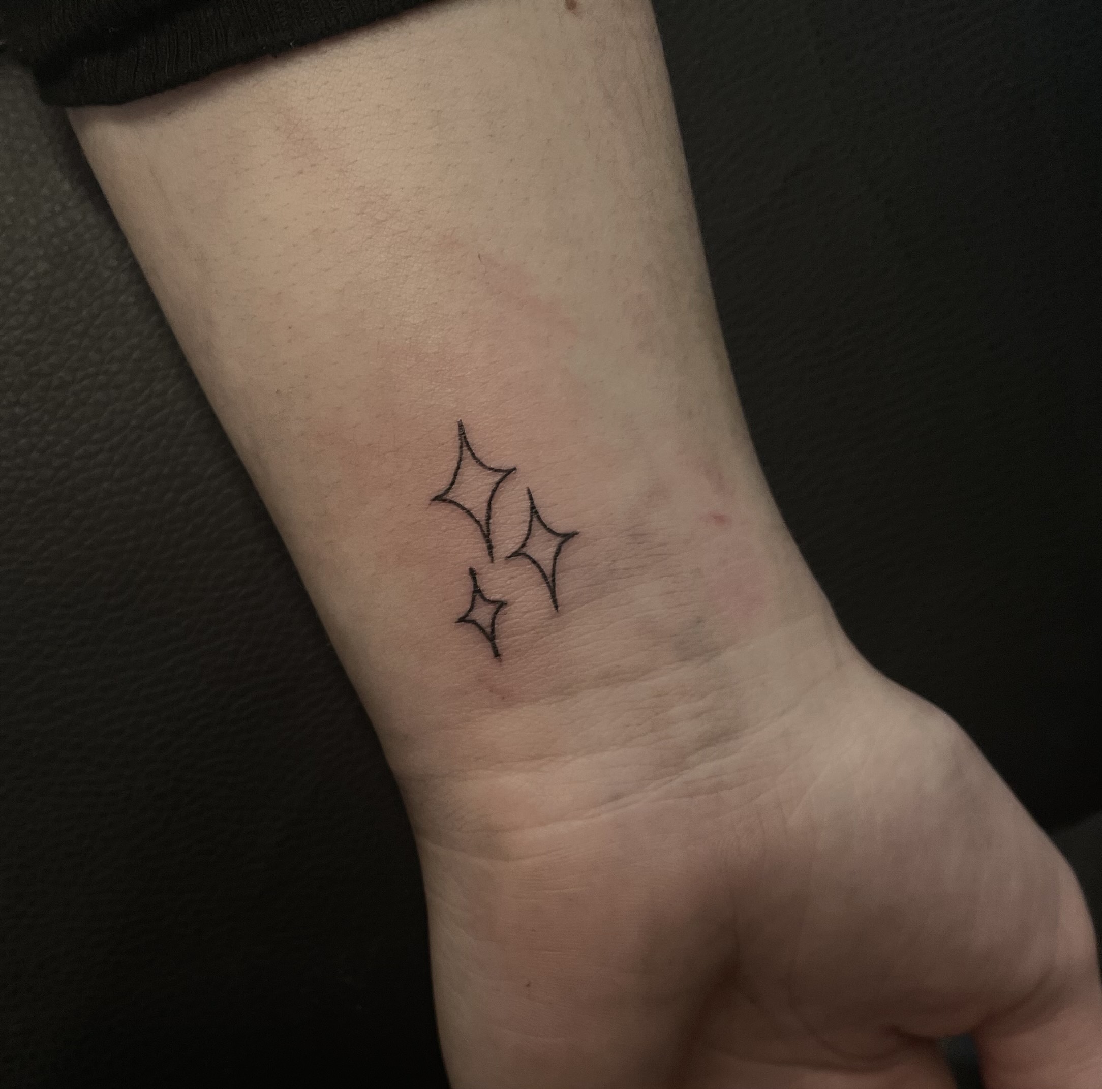 Image of a wrist with a fresh tattoo of three little stars in fineline style