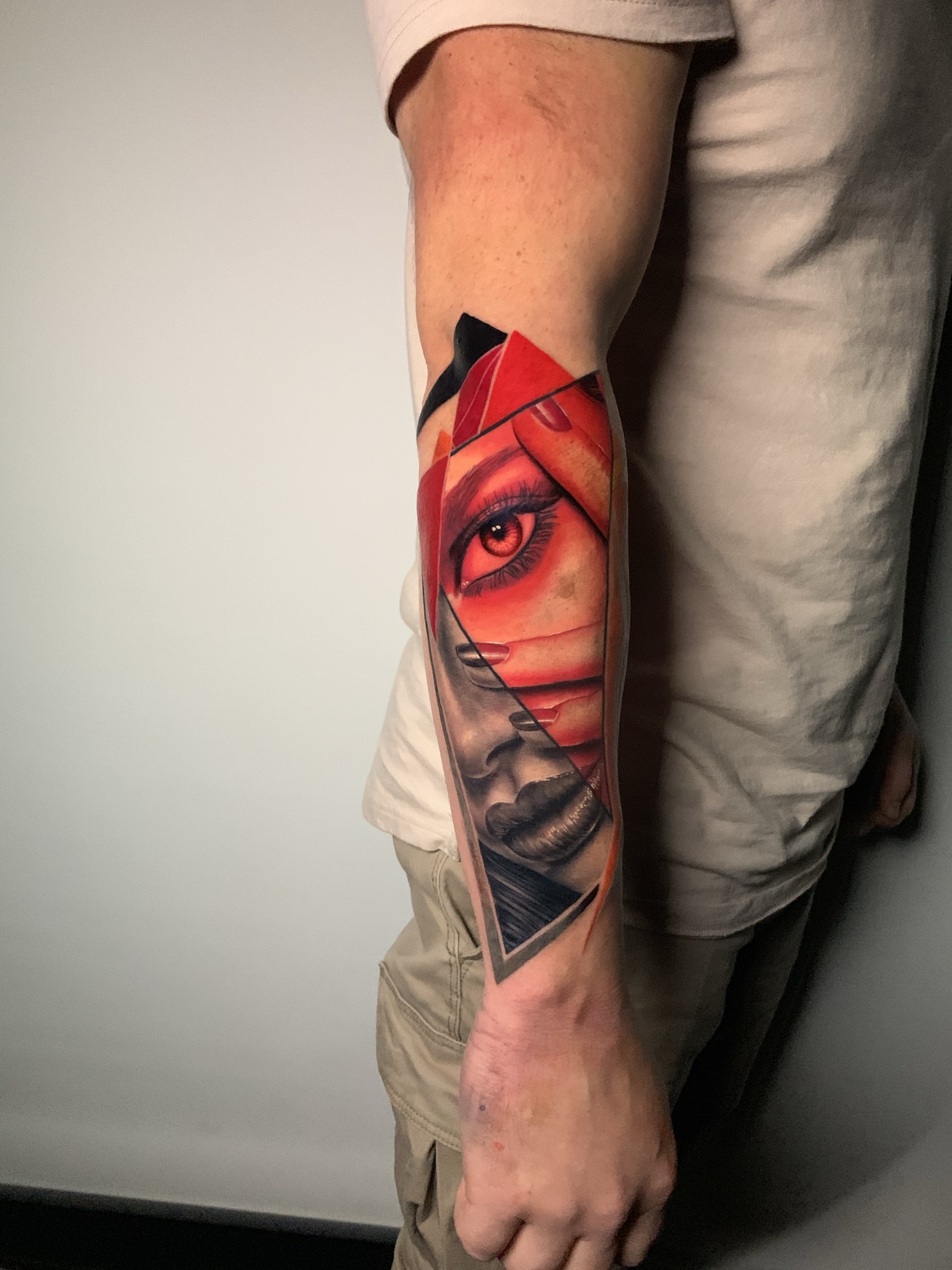 Image of a new tattoo on a mans arm. The style of the tattoo blends realism style with an artistic flair. It is black and grey and also red colour.